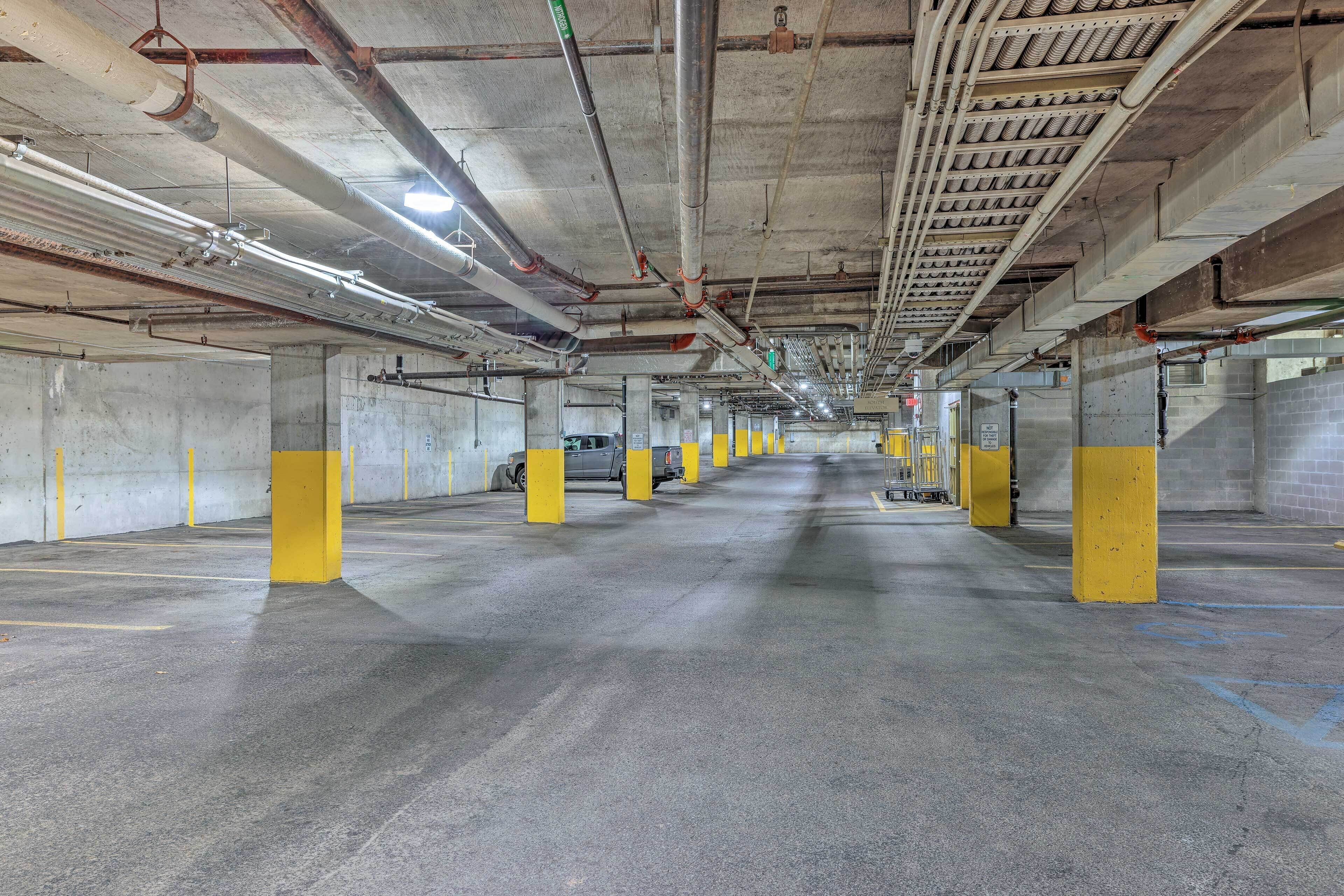 A multi-level parking garage with concrete floors, yellow pillars, and visible pipes on the ceiling.