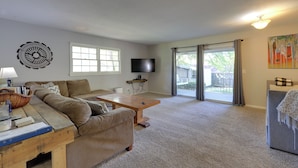 A living room with a sofa, coffee table, and TV. There is a window and a door leading outside. - 'the Ranger House' Columbus Home: Fenced Backyard (Columbus)
