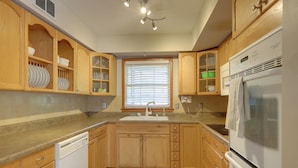 A kitchen with wooden cabinets, a dishwasher, a refrigerator, and a window with blinds. - 'the Ranger House' Columbus Home: Fenced Backyard (Columbus)