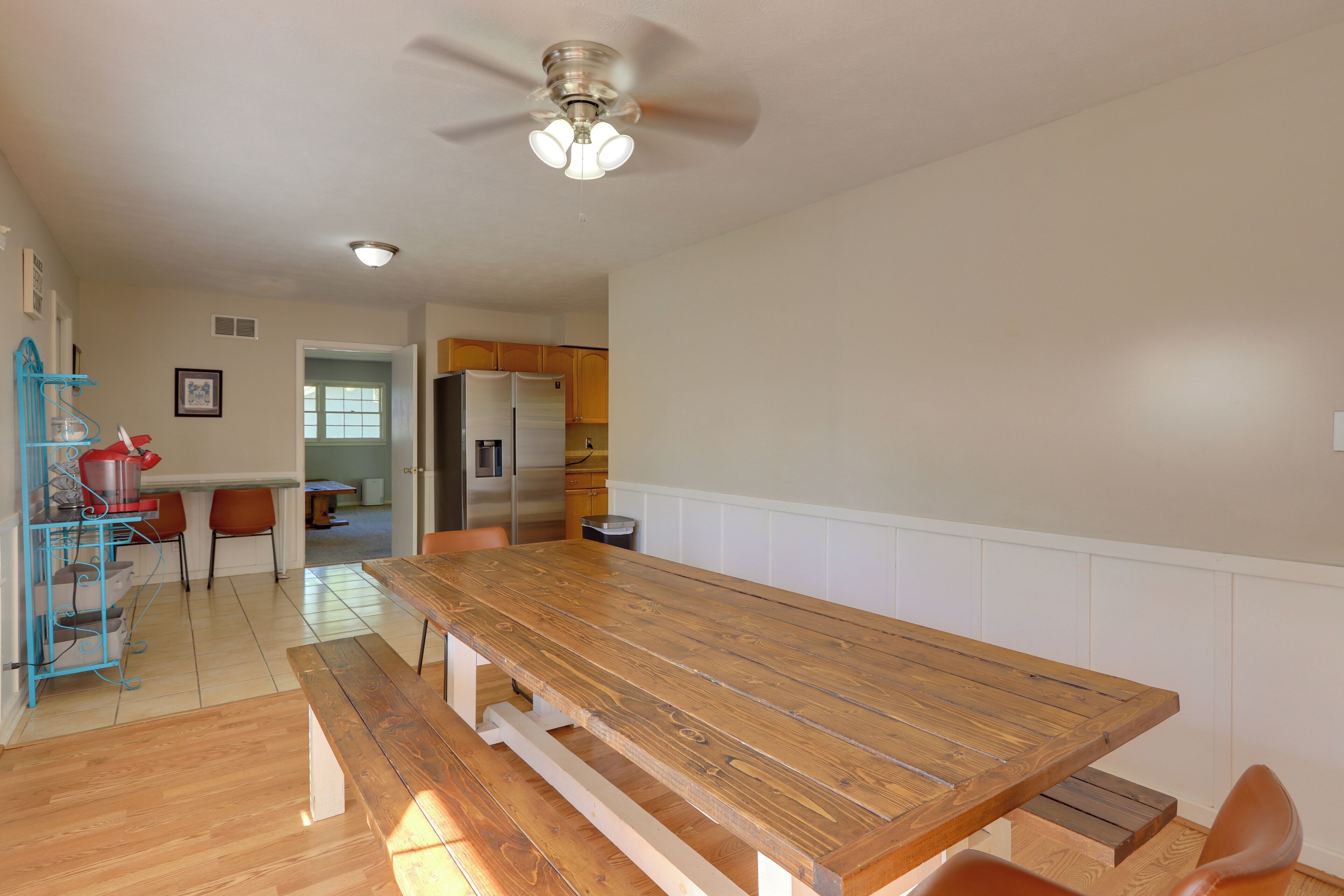 A spacious kitchen with a wooden dining table and benches, a ceiling fan, and a refrigerator.