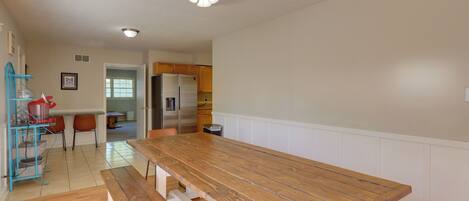 A spacious kitchen with a wooden dining table and benches, a ceiling fan, and a refrigerator.
