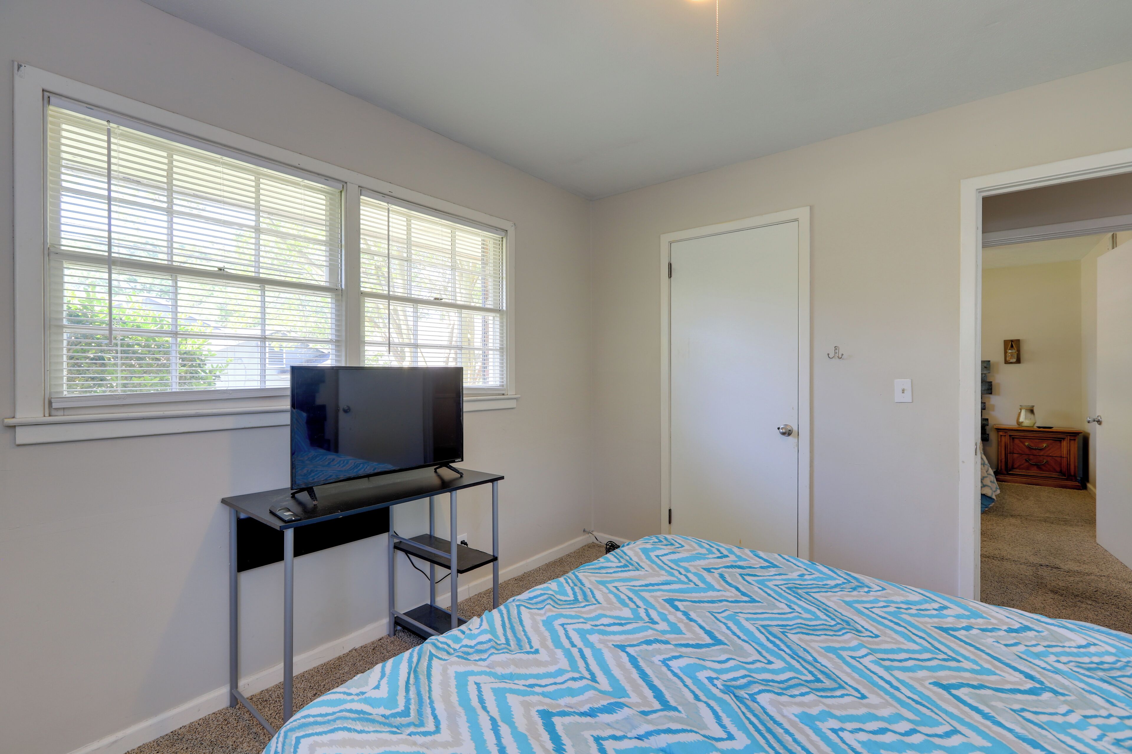A bedroom with a bed, a TV on a stand, and a door leading to another room.