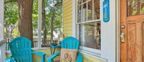 Une véranda avec deux fauteuils Adirondack turquoise et une porte en bois.