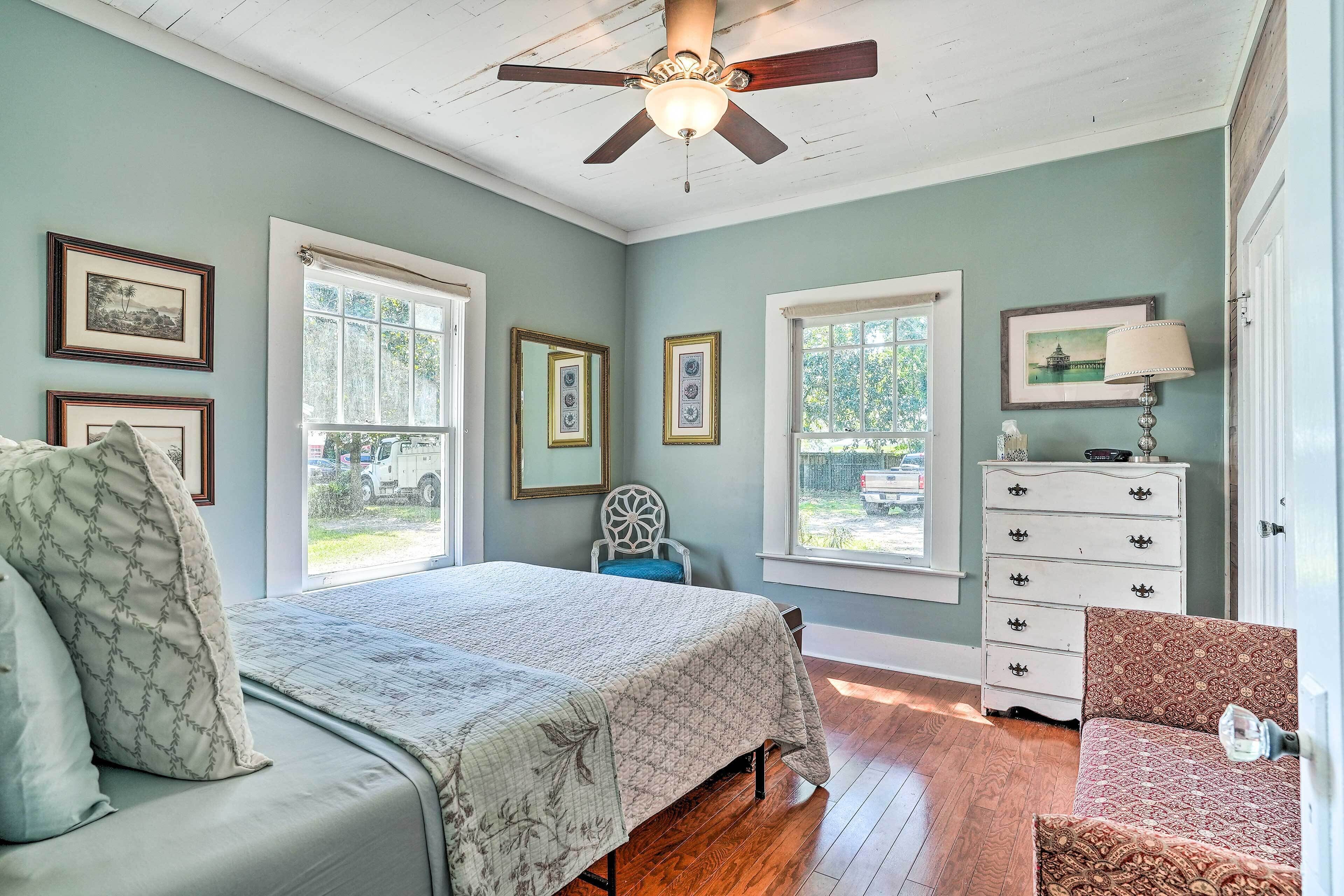 A bedroom with a bed, dresser, chair, and ceiling fan.
