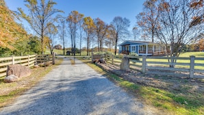 A gravel driveway leading to a house with a blue exterior and a wooden fence. - Modern Clarkesville Cottage w/ Decks & Patio! (Clarkesville)