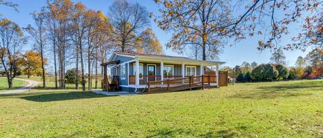 A single-story house with a porch, surrounded by a grassy yard and trees with autumn foliage.