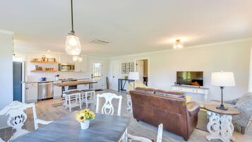 A spacious living area with a dining table, a brown leather sofa, and a television in the background.