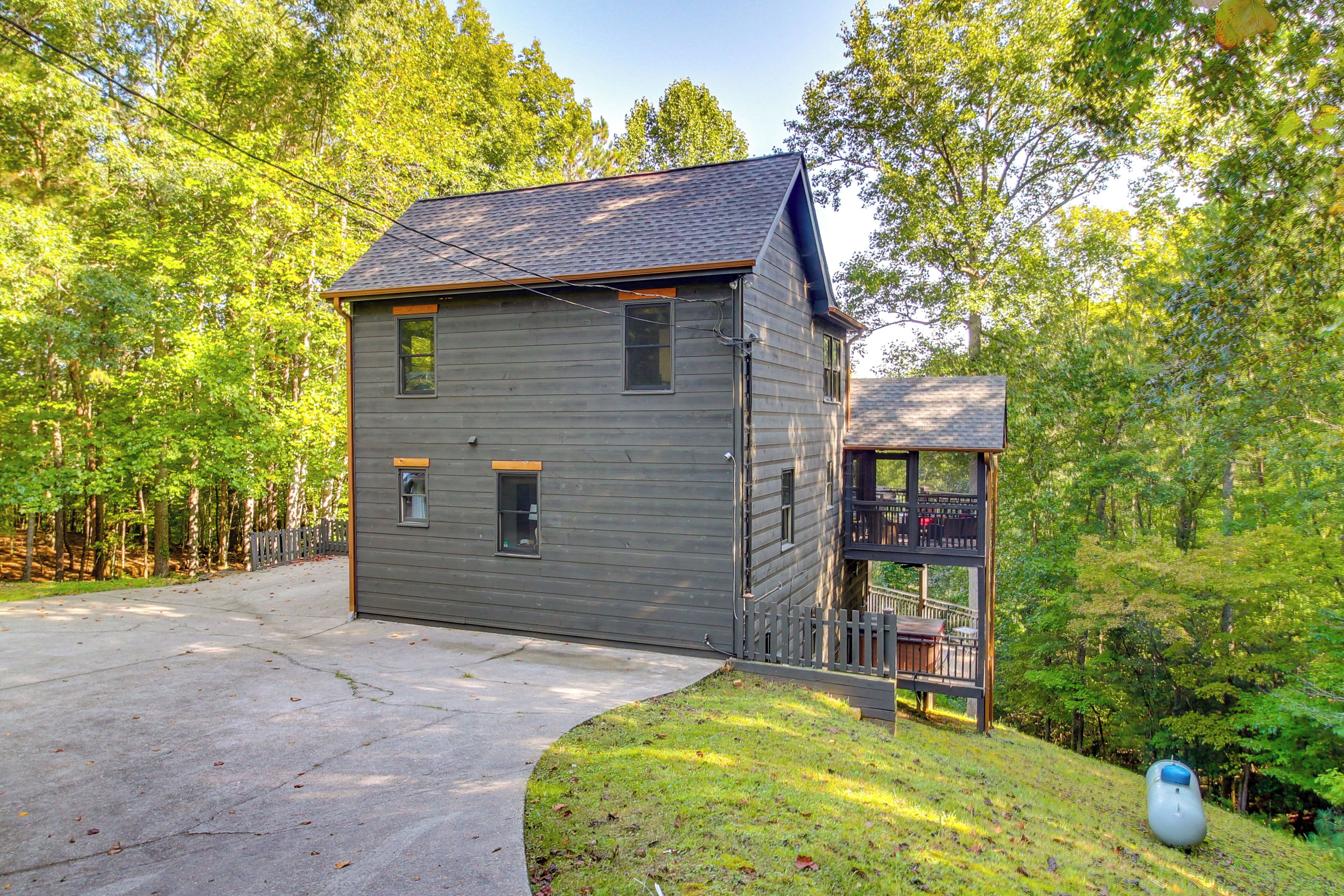 A two-story house with a front porch and a small deck, surrounded by a wooded area.