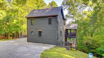 A two-story house with a front porch and a small deck, surrounded by a wooded area.