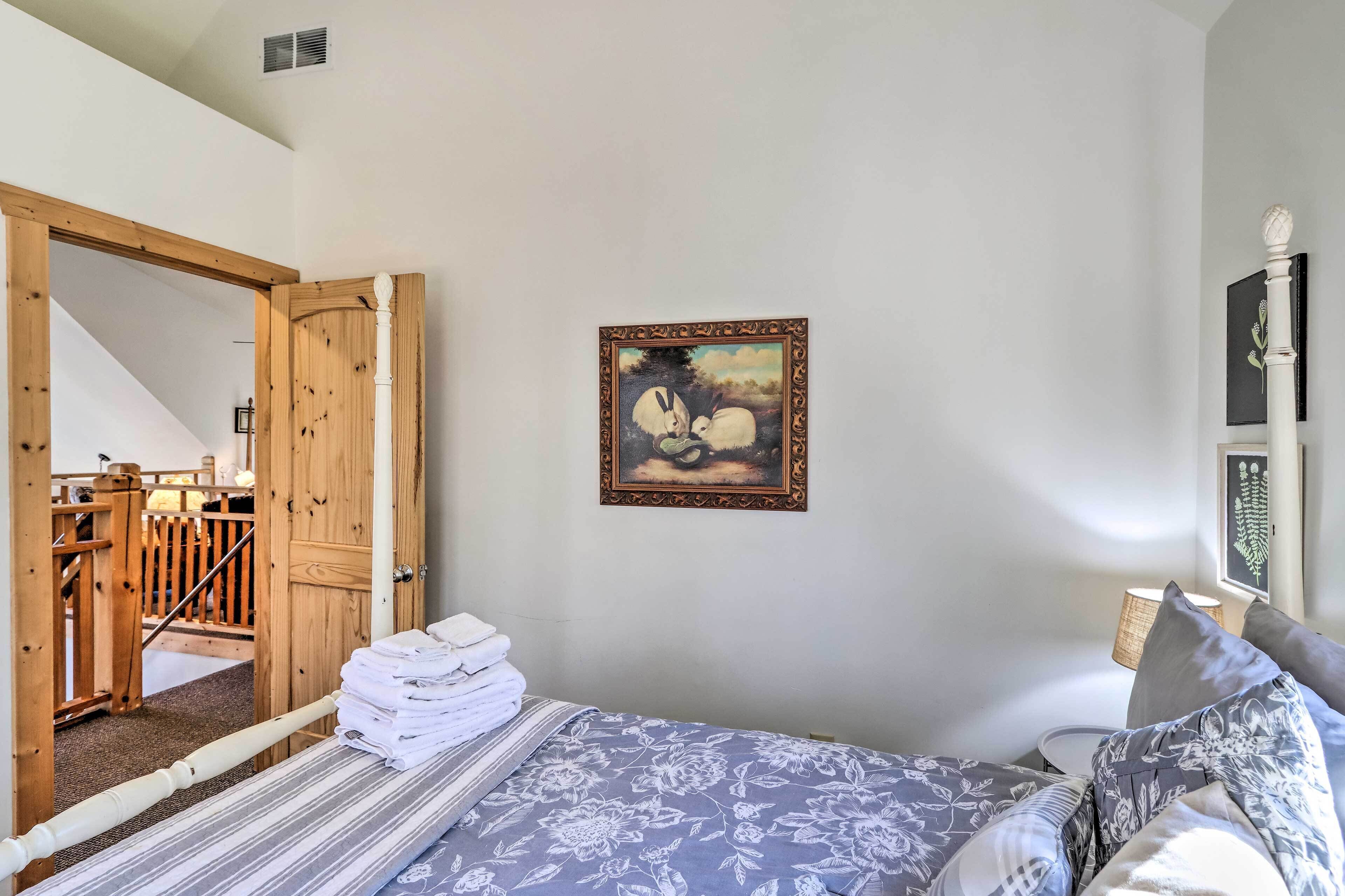 A bedroom with a bed, a painting, and a wooden door leading to a staircase.