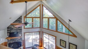 A loft-style room with a stone fireplace, large windows, and a ceiling fan. - Spacious Ellijay Resort Home w/ Hot Tub! (Ellijay)