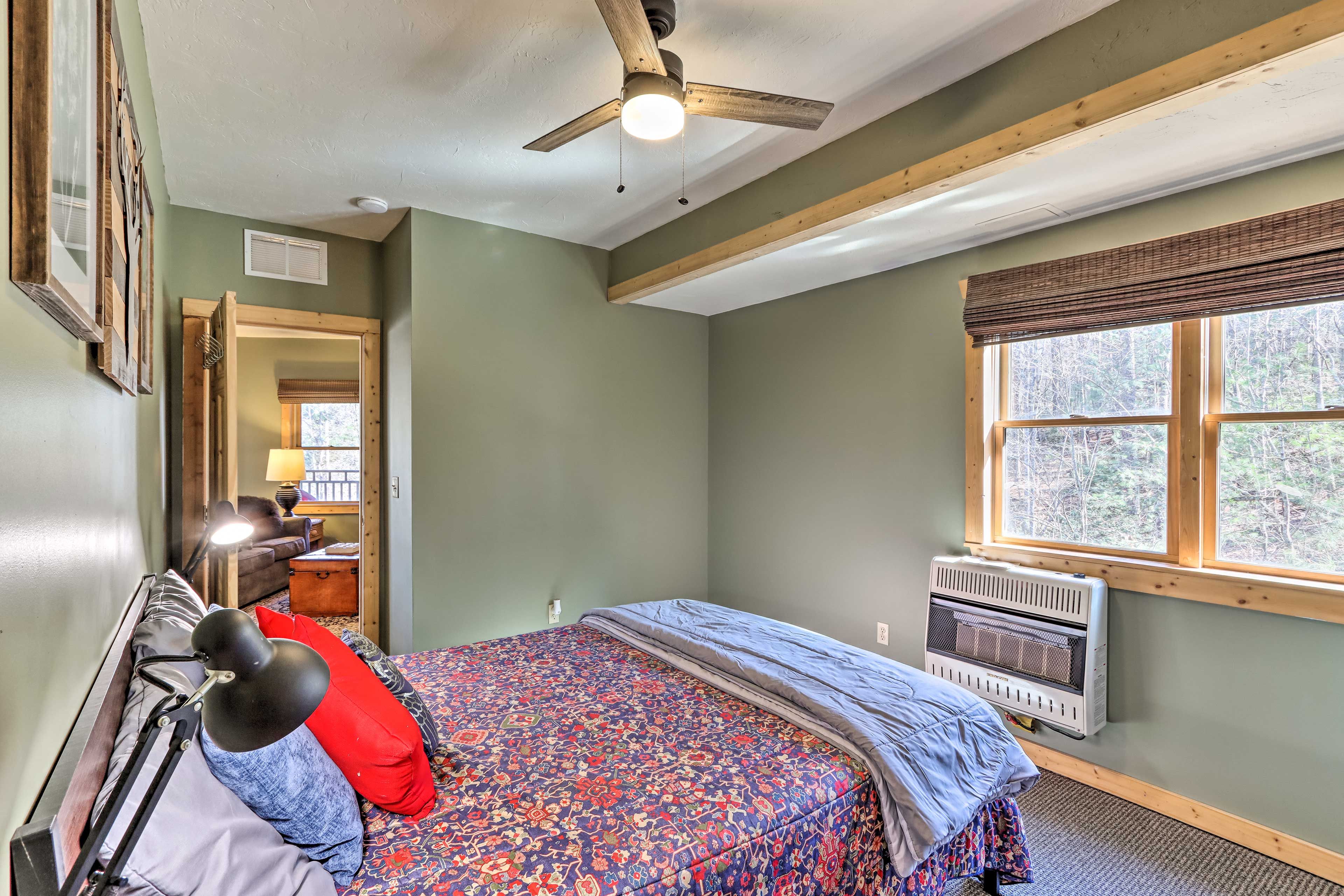 A bedroom with a bed, a ceiling fan, a heater, and a window with a view of trees.