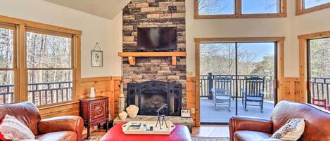 A cozy living room with a stone fireplace, leather sofas, and a large window overlooking a deck.