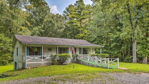 A small, single-story cabin with a porch, surrounded by lush greenery and a flag.