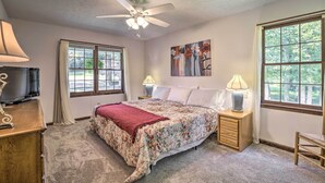 A bedroom with a bed, a ceiling fan, a TV, and two windows.