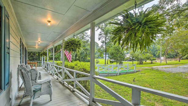 A covered porch with wicker furniture and a view of a grassy area with a white fence and a bench.