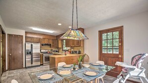 A modern kitchen with wooden cabinets, a stainless steel refrigerator, and a dining area with a glass table and chairs.