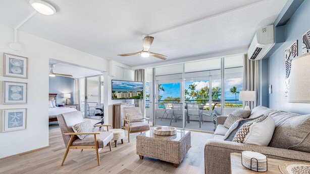 A spacious living area with a large window overlooking a scenic ocean view, a ceiling fan, and a modern interior design. - June Specials! Beautiful Stylish Condo W/ Amazing Ocean Views! (Kihei)