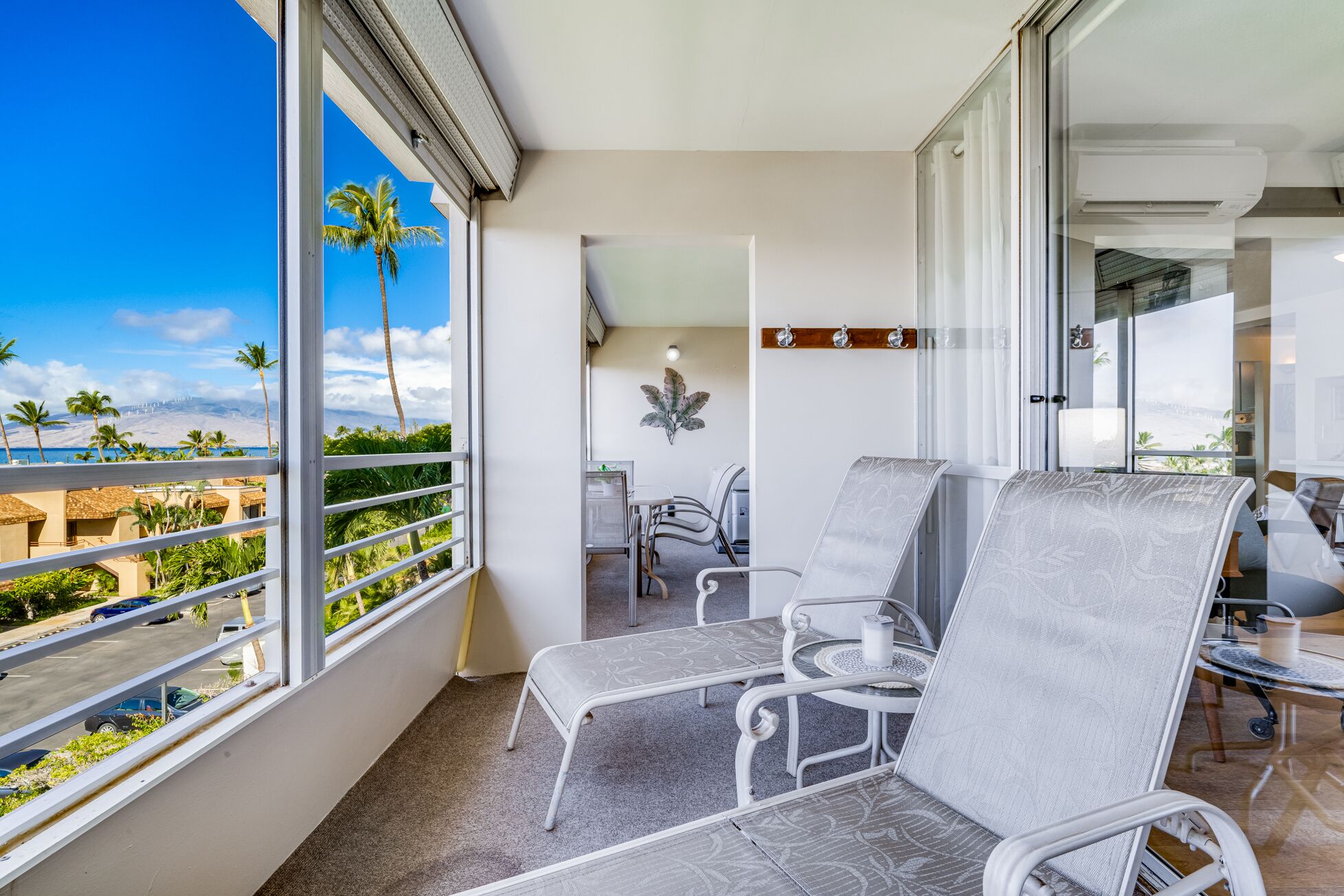 Un balcon avec deux fauteuils gris rembourrés, une petite table et une vue sur une plage et des palmiers.