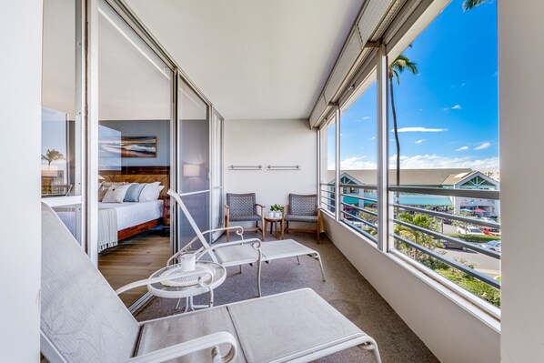 A balcony with a bed, two chairs, and a small table. - June Specials! Beautiful Stylish Condo W/ Amazing Ocean Views! (Kihei)