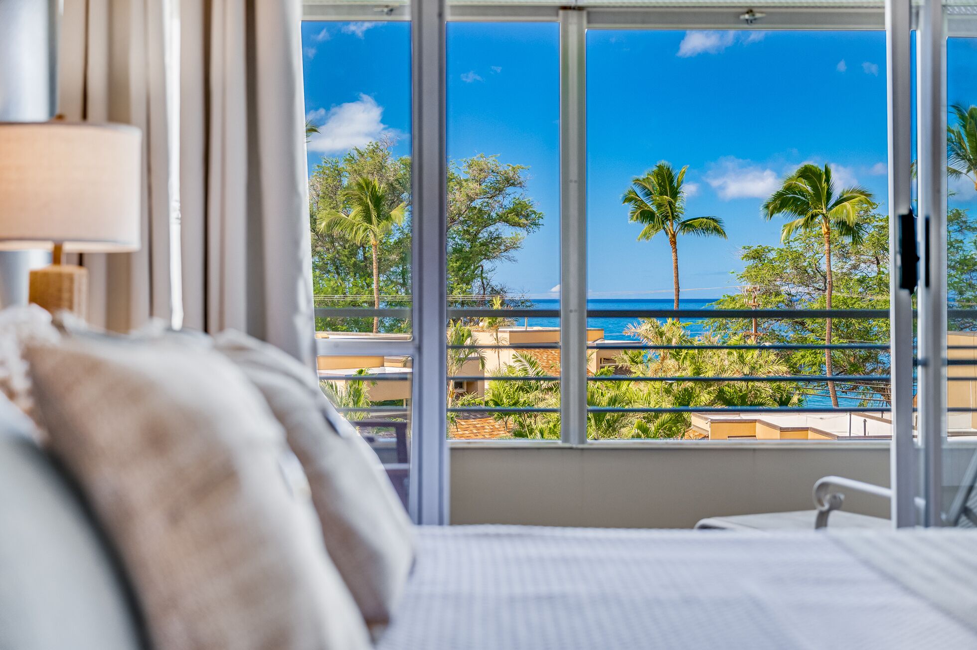 Een hotelkamer met een groot raam en uitzicht op de oceaan en palmbomen.