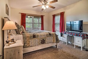 Ein Schlafzimmer mit Bett, Schreibtisch, Fernseher, Deckenventilator und einem Fenster mit Vorhängen.