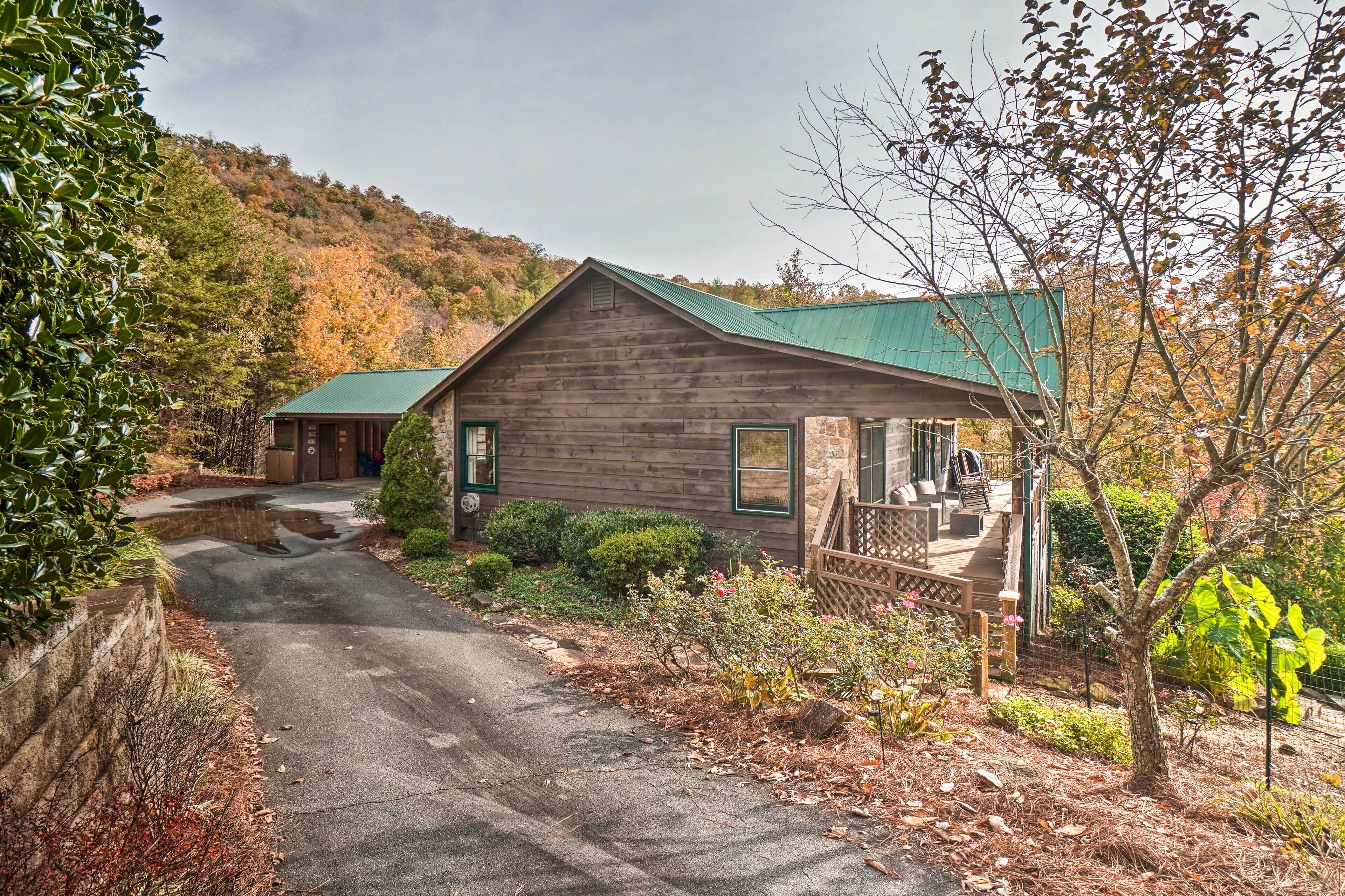 A rustic cabin with a green roof, surrounded by autumn foliage and a stone pathway leading to the entrance.