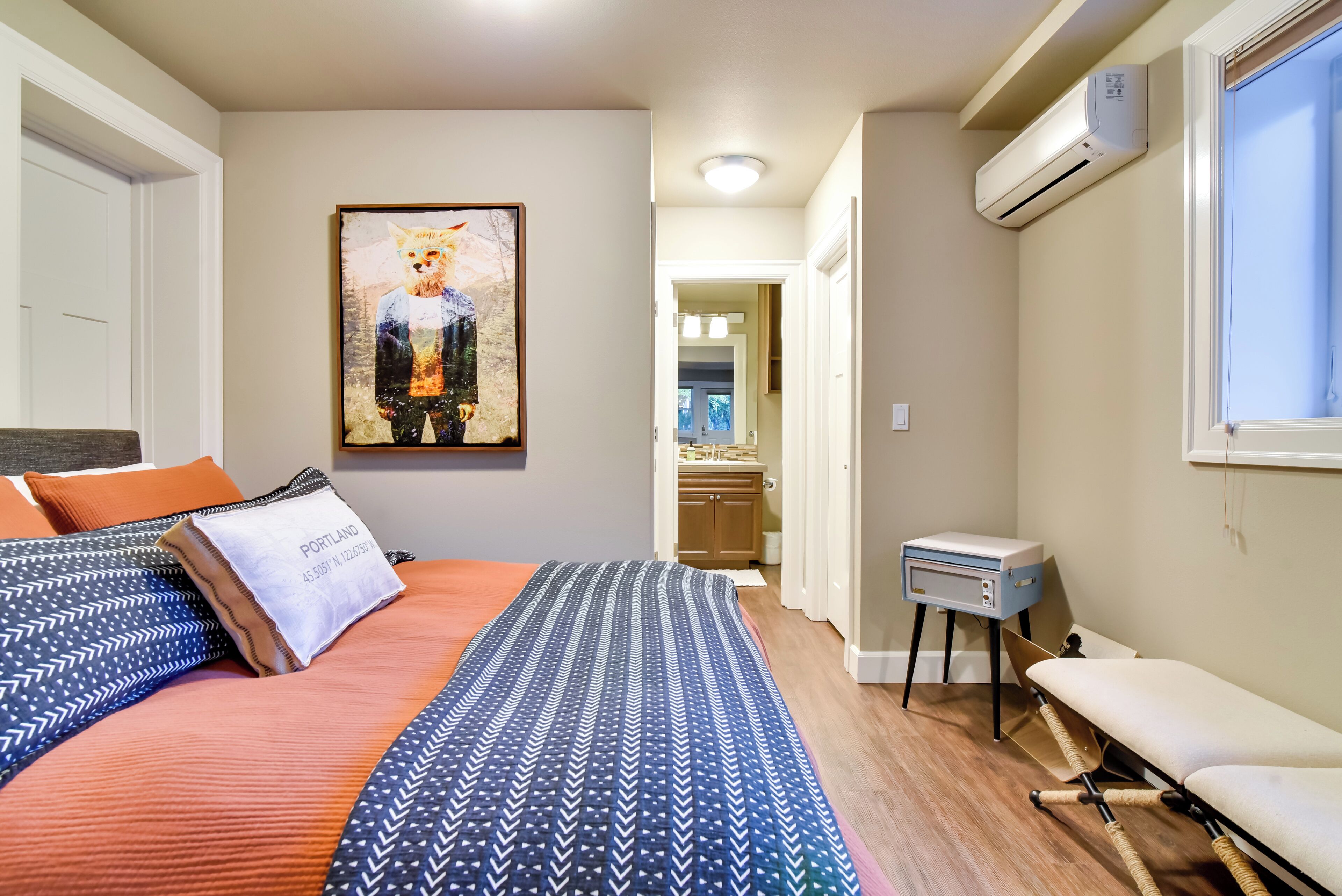 Un dormitorio con una cama, un cuadro, un aire acondicionado y una mesita.