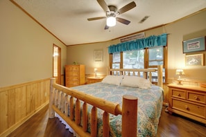 A bedroom with a wooden bed, a ceiling fan, a window with curtains, a nightstand, and a dresser.