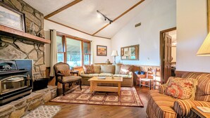 A cozy living room with a stone fireplace, wooden furniture, and large windows. - Mountain Resort Home w/ Views, By Sky Valley Golf! (Dillard)