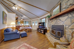 A cozy living room with a fireplace, wooden floors, a blue sofa, a television, and a dining area with a table and chairs.