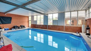 An indoor swimming pool with a brick wall, large windows, and a metal roof.