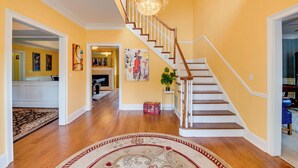 A spacious foyer with a wooden staircase, a chandelier, and a large rug.