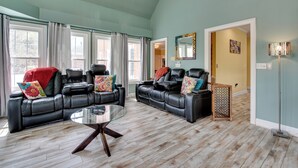 A spacious living room with a sectional sofa, a glass coffee table, and a large window with curtains.