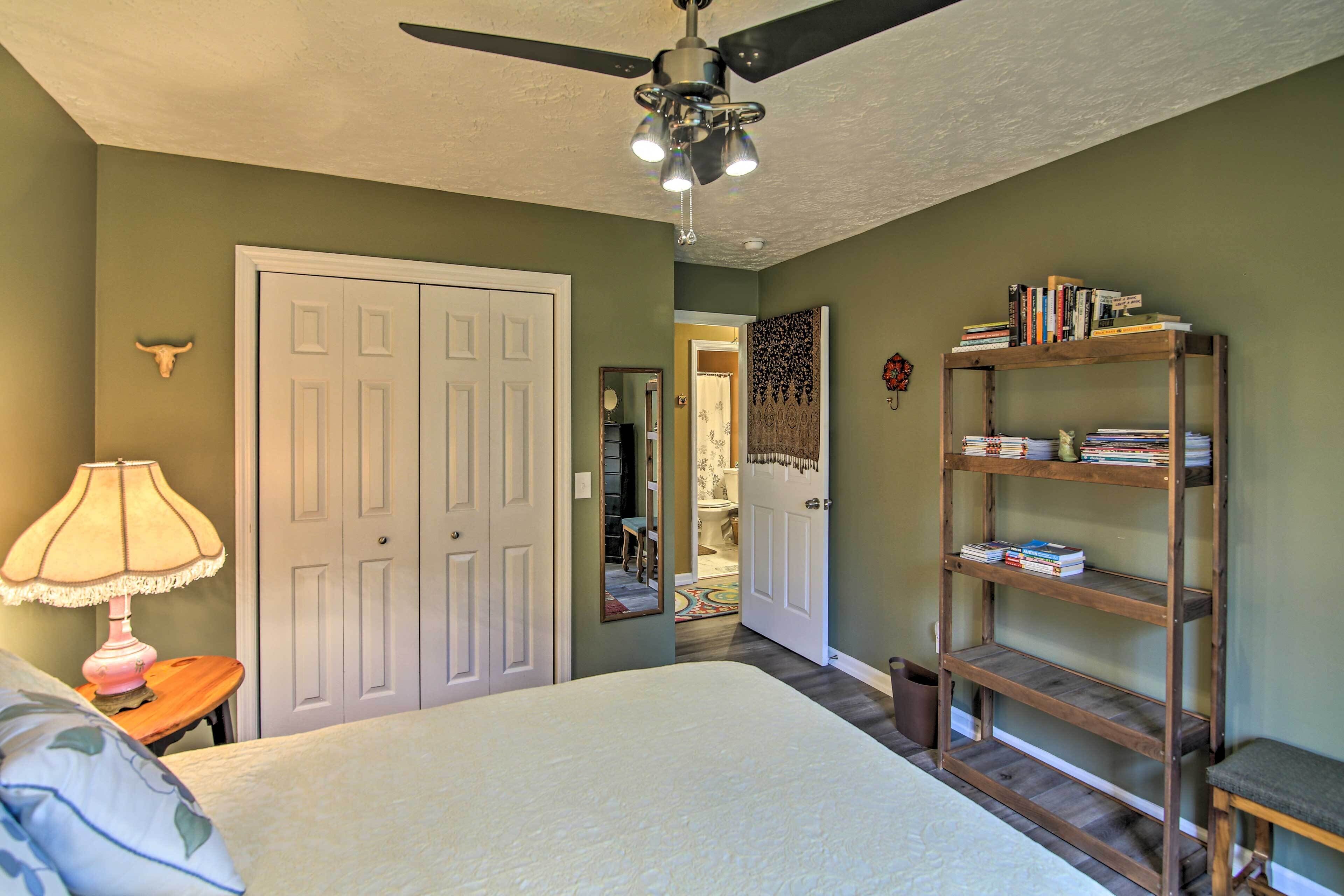 A bedroom with a bed, a ceiling fan, a bookshelf, and a door leading to another room.