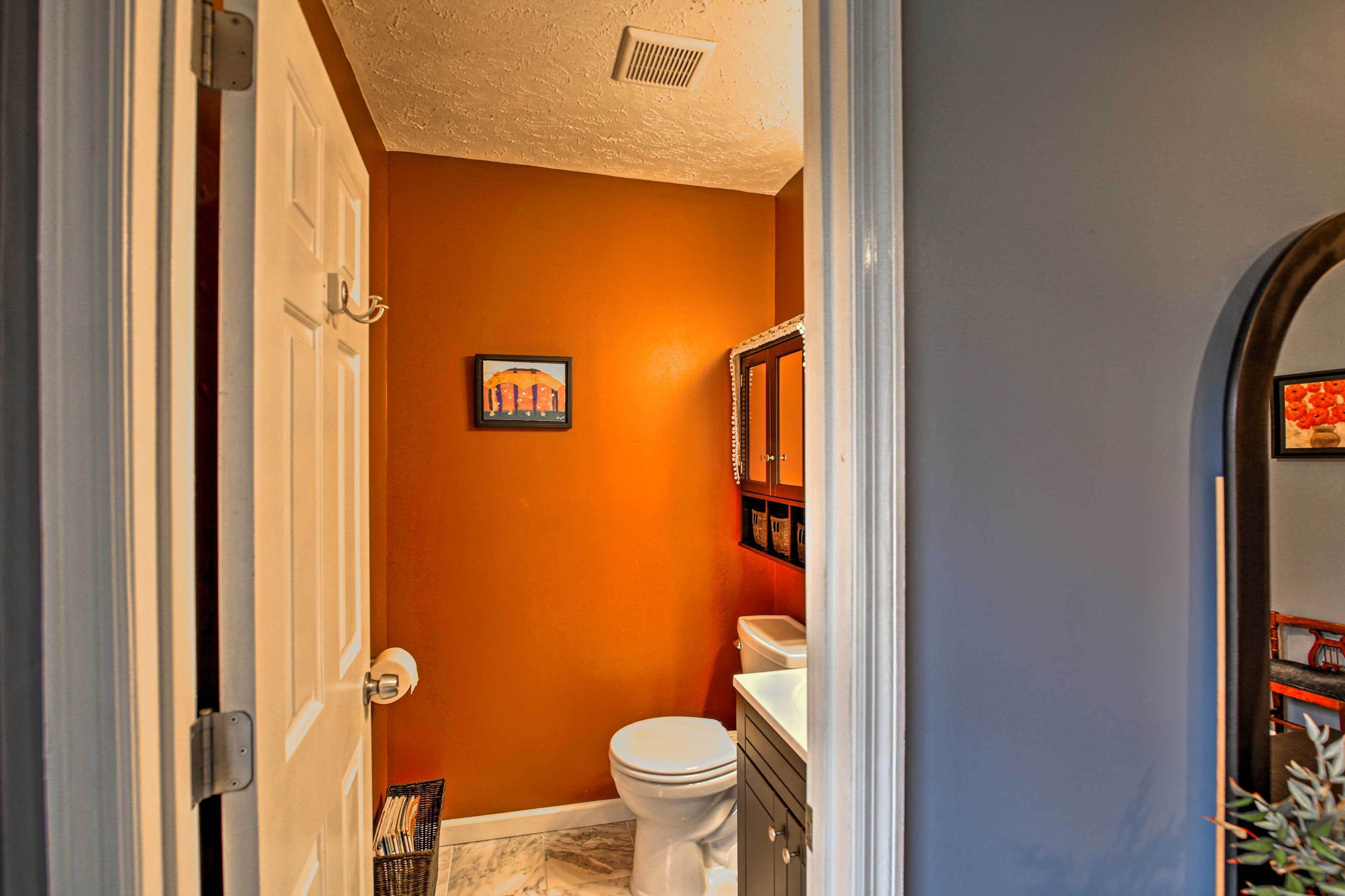 A bathroom with an orange wall, a white toilet, a sink, and a mirror.