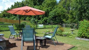 An outdoor patio with a table and chairs, a red umbrella, and a garden area with plants and a bird bath. - Lively East Nashville Pad: Walk to Bars & Eateries (Nashville)