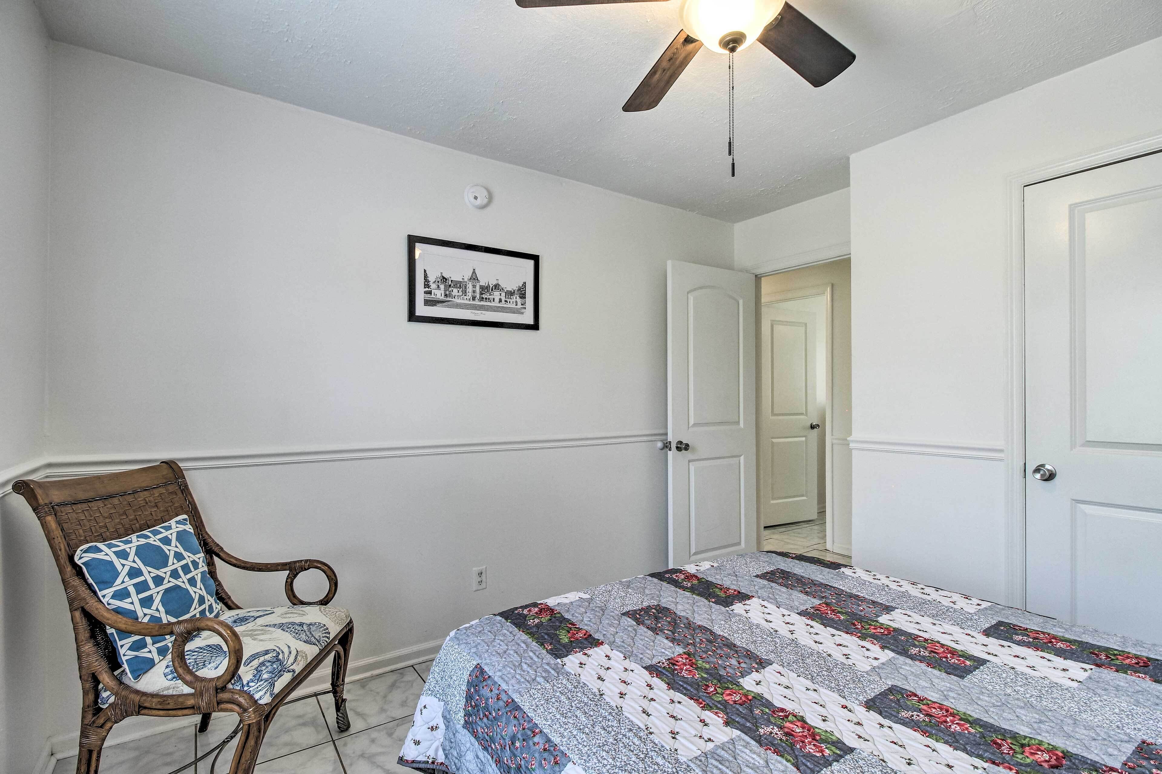 Une chambre à coucher avec un lit, une chaise, un ventilateur de plafond, une porte et un tableau encadré au mur.