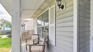 Une véranda avec deux chaises et une table, une balustrade en bois, et une maison avec un revêtement extérieur blanc et des volets.