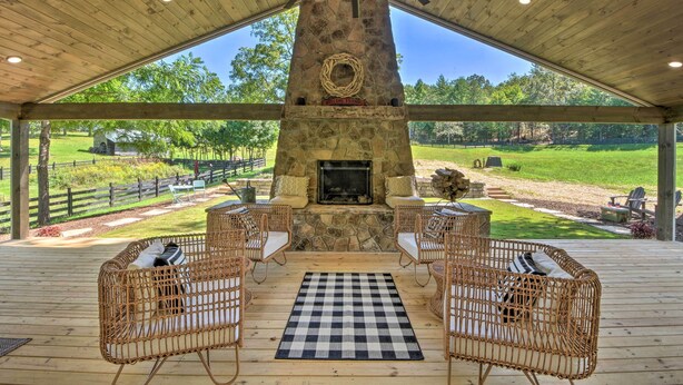 A covered outdoor area with a stone fireplace, wicker furniture, and a checkered rug. - Blue Ridge Cottage: Modern Solace in the Mountains (Blue Ridge)