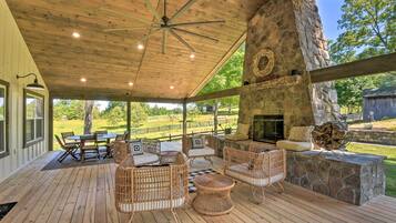 A covered patio with wicker furniture, a stone fireplace, and a view of the outdoors.