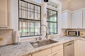 A kitchen with a granite countertop, a stainless steel sink, a microwave, and white cabinetry.