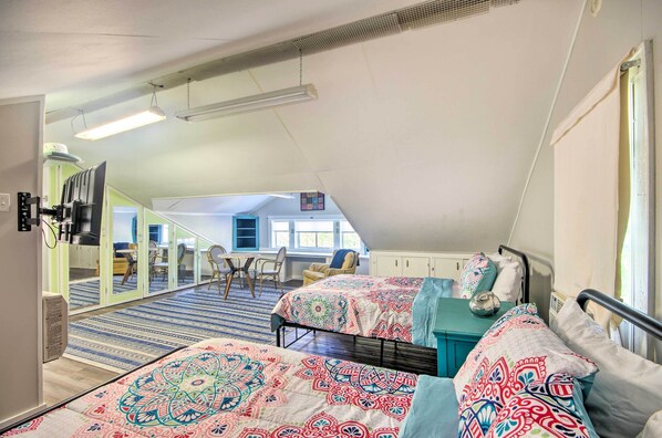 A bedroom with two beds, a desk, and a chair in a loft-style room with a view.