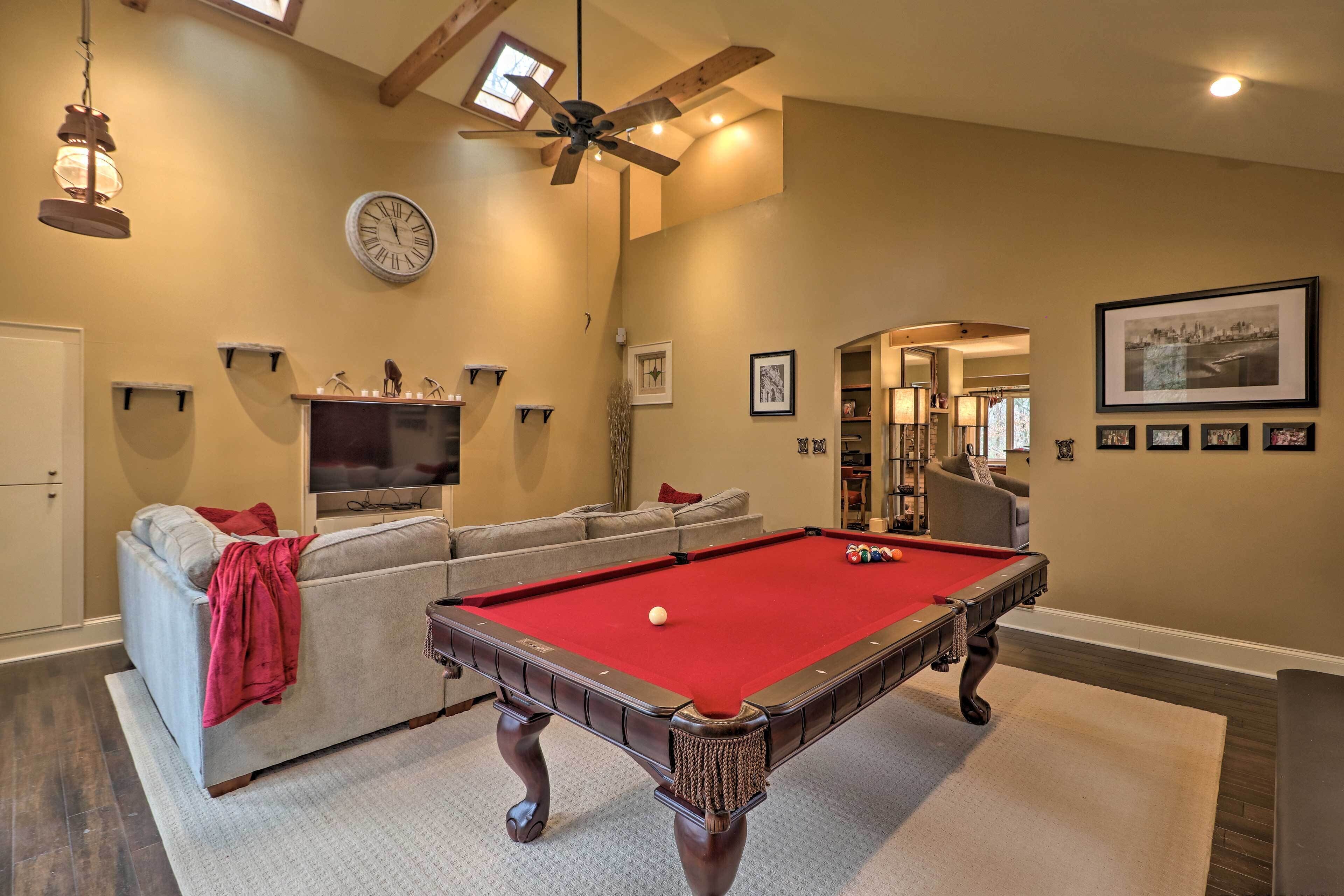 A pool table in a living room with a sofa, a ceiling fan, a clock, and framed pictures on the wall.