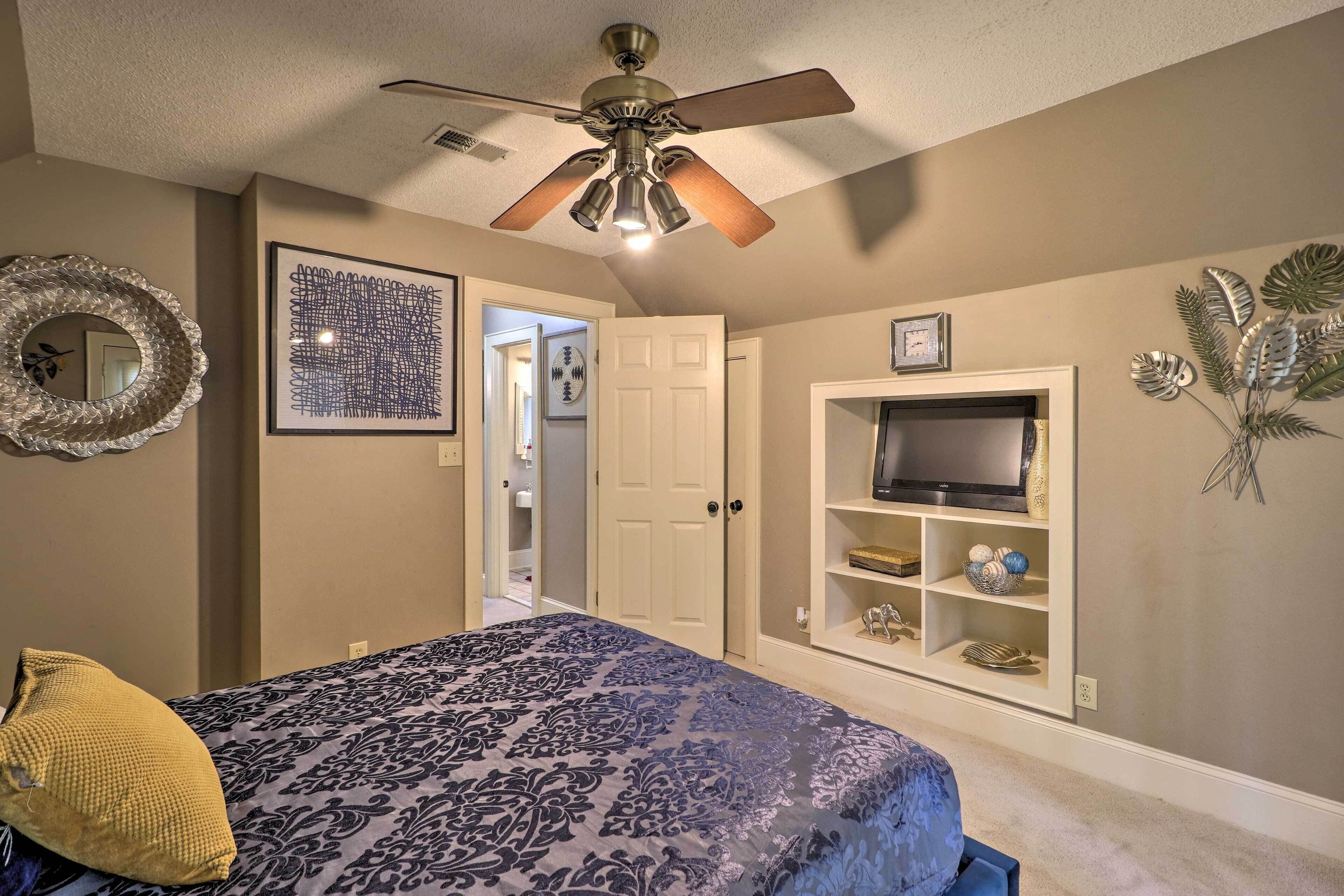 A bedroom with a bed, ceiling fan, TV, and decorative items.