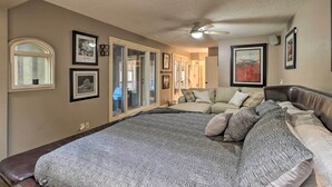A bedroom with a large bed, a ceiling fan, and a view of the living area through glass doors. - Cozy Conyers Cabin w/ Fireplace & Pool Table! (Conyers)