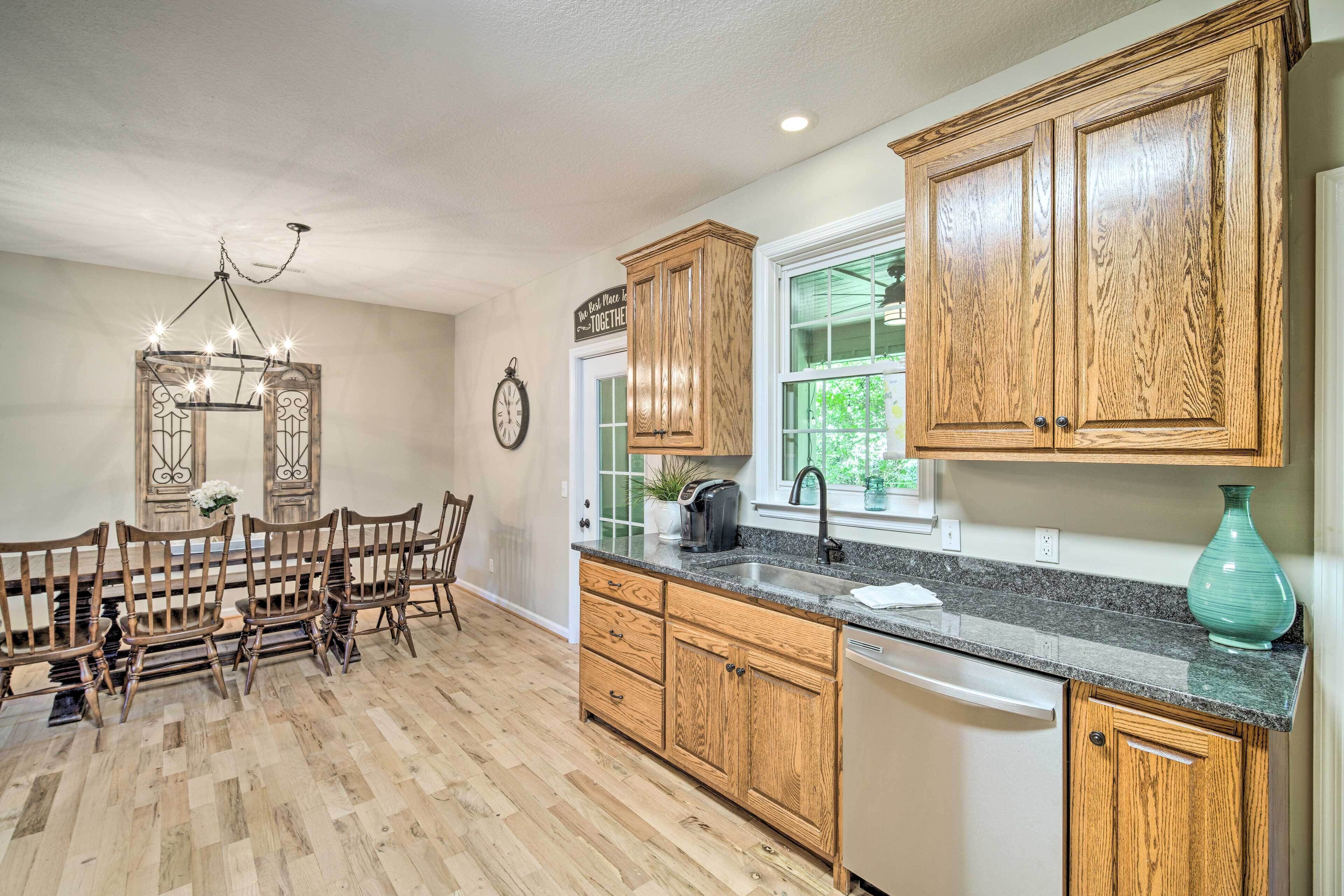 A kitchen with wooden cabinets, a granite countertop, and a dining area with wooden chairs.