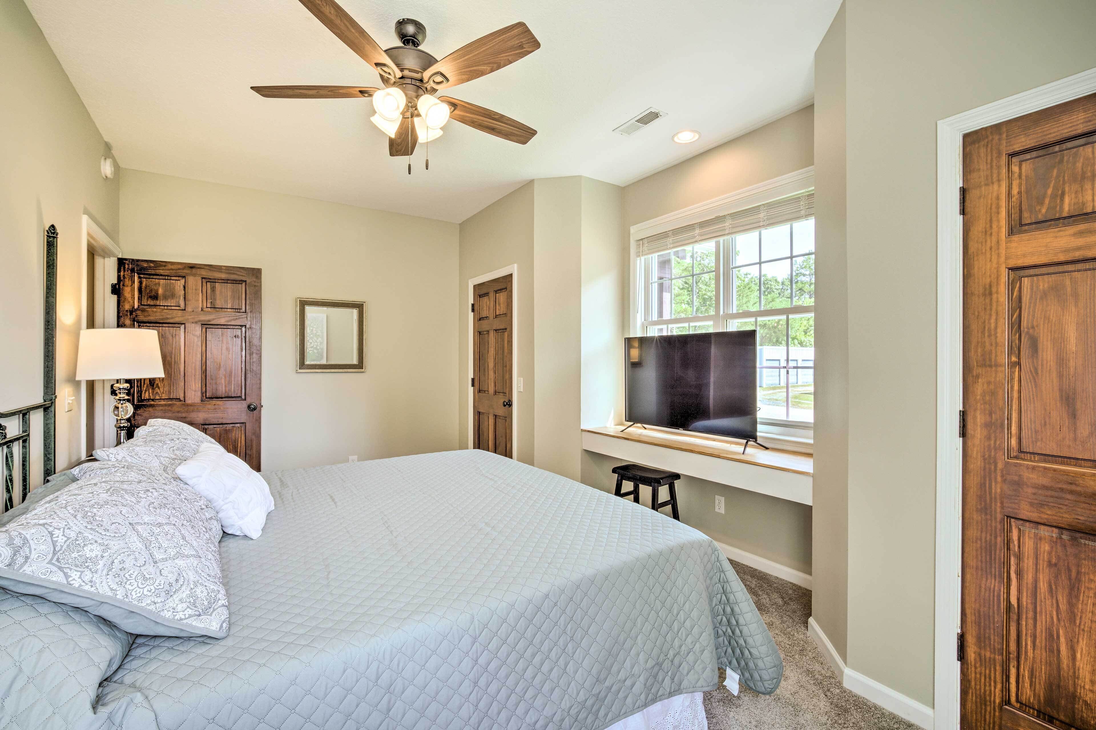 A bedroom with a bed, a ceiling fan, a window with blinds, and a door.