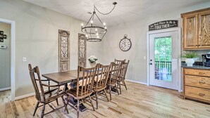 Un comedor con mesa y sillas de madera, una araña, un reloj y una puerta que da a un balcón.