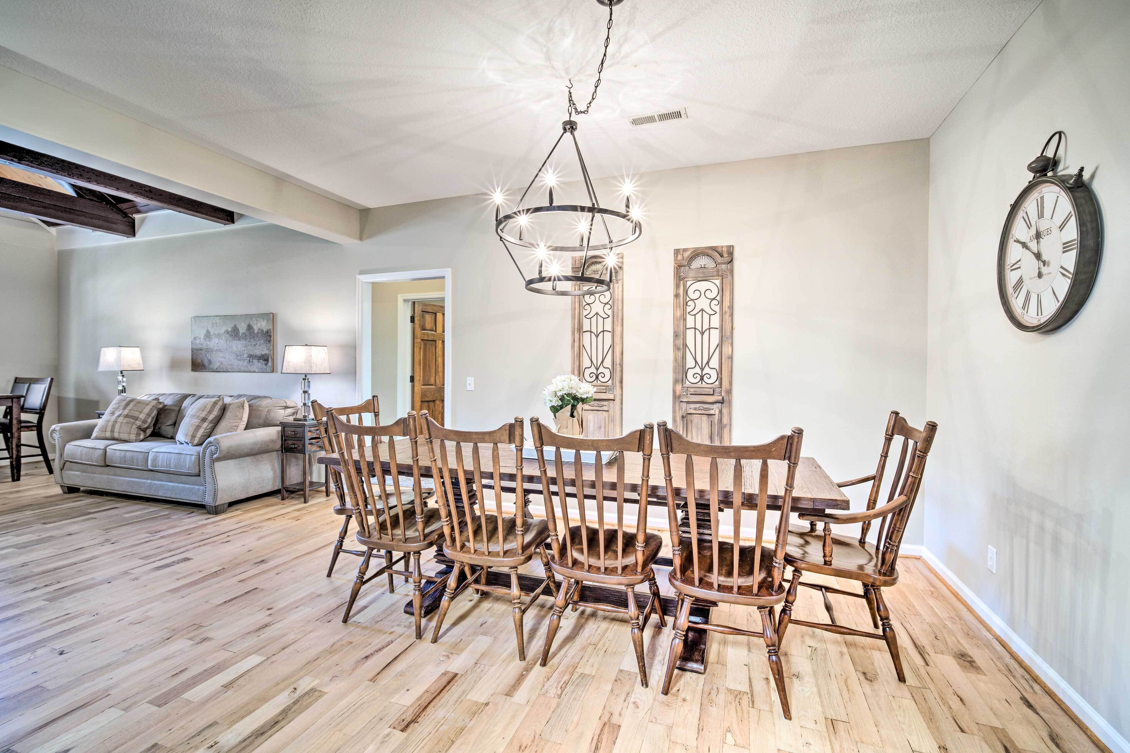A dining area with a wooden table and chairs, a chandelier, and a wall clock.